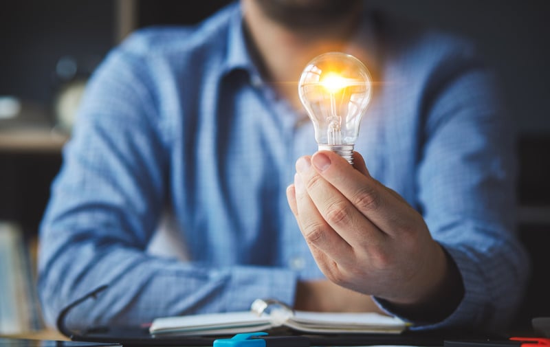 A person holding a glowing lightbulb above an open notebook